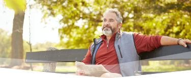 Banner photo at the top of the page showing a man sitting on a park bench, glancing up from his newspaper to take in the scenery of beautiful day at the park.  