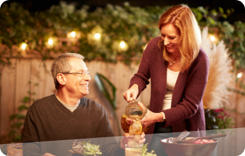 Photo of a man hosting a backyard barbecue, being served iced tea as he sits down to dinner.  