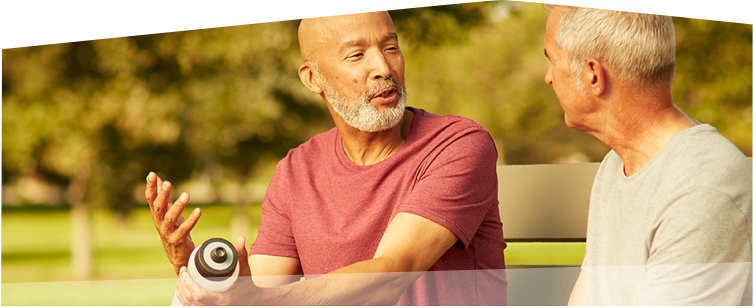 Photo of two men wearing athletic clothing and having a friendly conversation with each other while sitting on a park bench.  