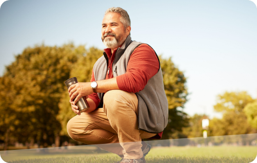 Photo of a man enjoying time in the park on a beautiful fall day. He’s crouching down on a patch of grass, taking in the scenery. 