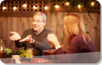 Photo of a man hosting a backyard barbecue and having a lively conversation at the dinner table. 
