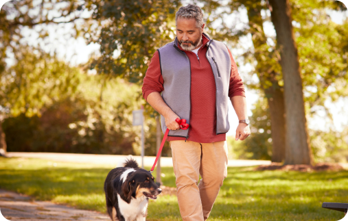 Photo of a man looking affectionately at his dog as they walk together down a park path on a beautiful fall day.