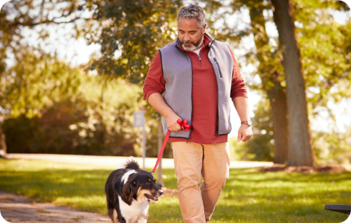 Photo of a man looking affectionately at his dog as they walk together down a park path on a beautiful fall day. Photo of a man looking affectionately at his dog as they walk together down a park path on a beautiful fall day.