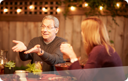 Photo of a man hosting a backyard barbecue and having a lively conversation at the dinner table.